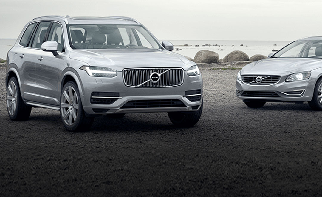 Volvo XC90 und Volvo V40 stehen nebeneinander vor einem See – Vorderansicht